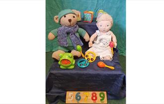 A teddy and doll surrounded by rattles and toys