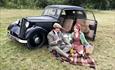Couple dressed in vintage clothes whilst enjoying a picnic next to their old car