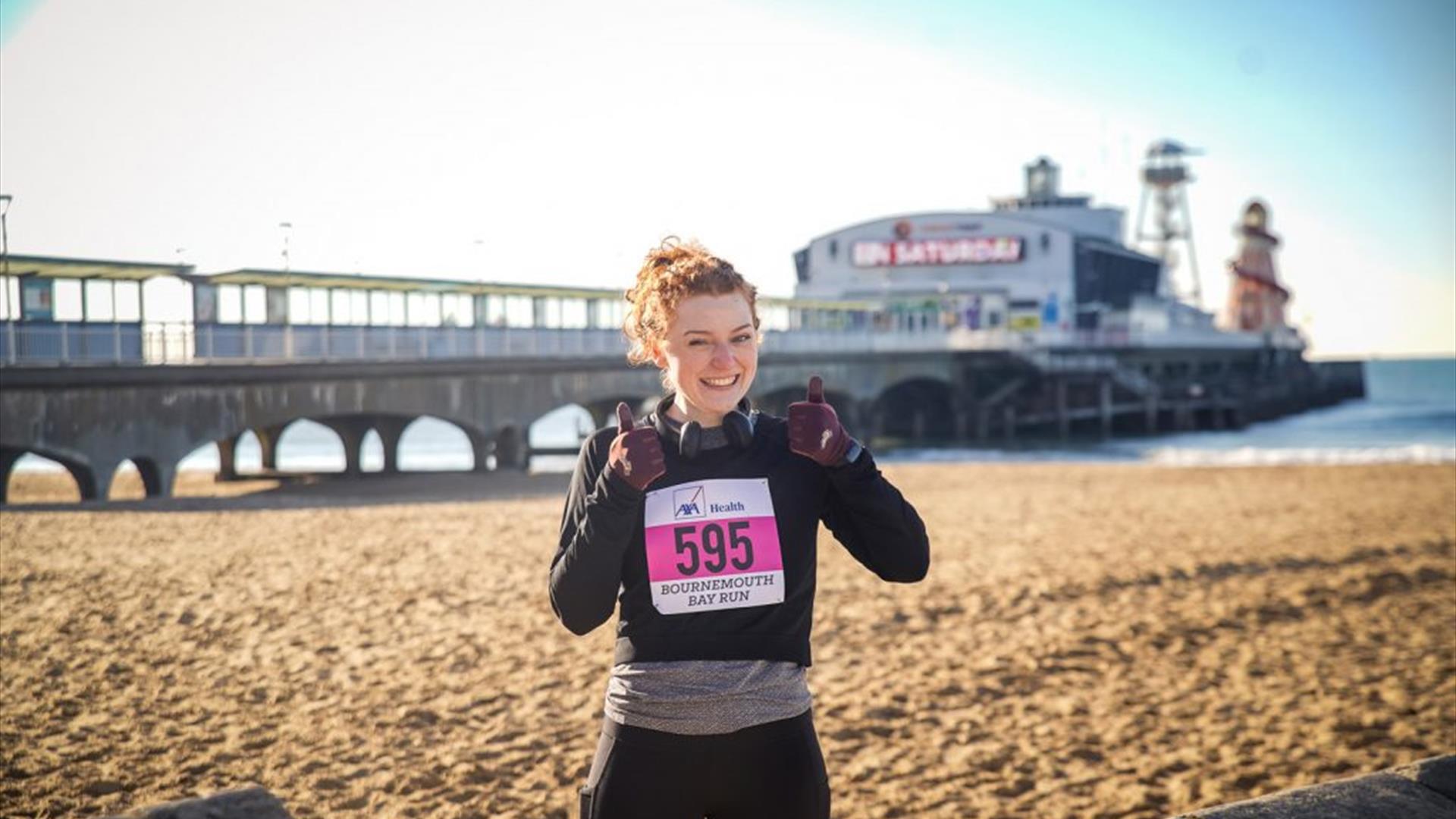 Woman runner with her thumbs up smiling at the camera next to Bournemouth beach
