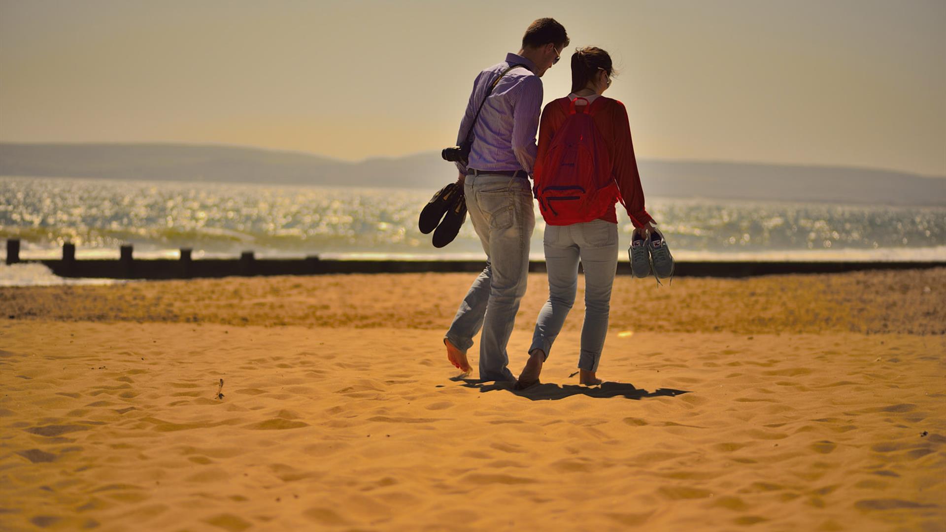 Couple walking in the sand surrounded by ornage light from the sun