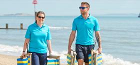 Two seafront rangers wearing their iconic blue polos walk along Bournemotuh beach collecting deckchairs