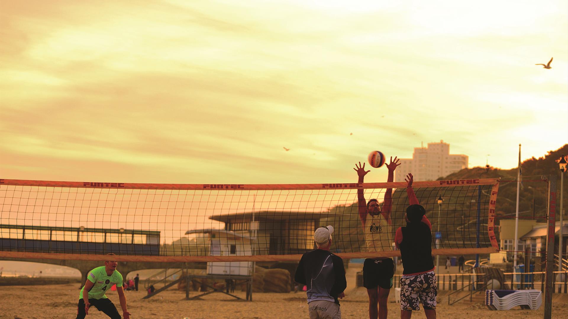 Friends playing volleyball on the beach as the sun is setting