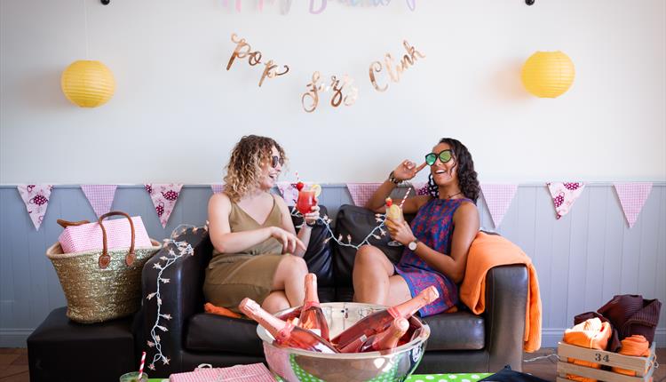 Two venue guests laughing and drinking on a sofa inside the decorated venue