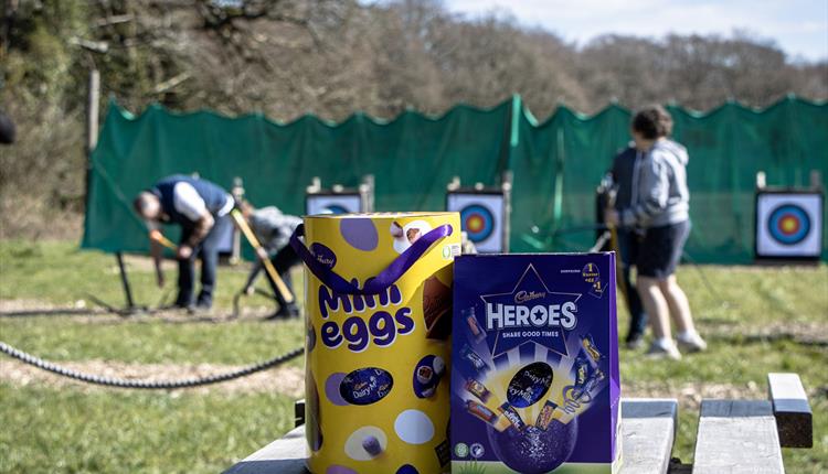 Two easter eggs on a bench in front of children doing archery.