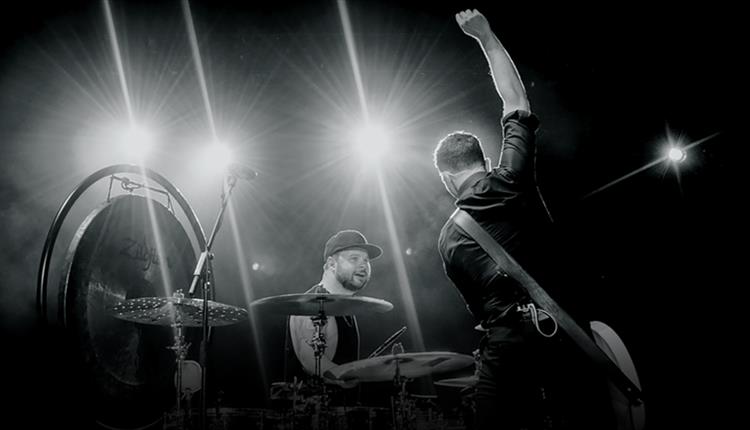A black and white image of two men performing, one signing and one playing the drums.