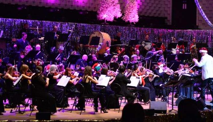 A orchestra on stage with a conductor at the front with a Santa hat on