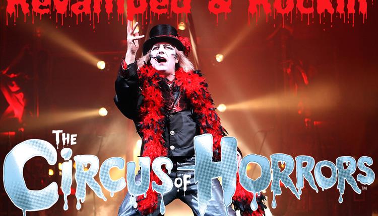 Man dressed in black and red with stage lights behind him and a logo of the Circus of Horrors