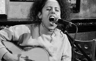 Black and white image of female spanish singer up close to microphone and playing the guitar
