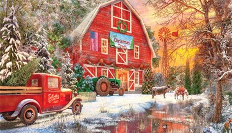 A red barn with a green tractor outside with snow on the ground and two cows in the background