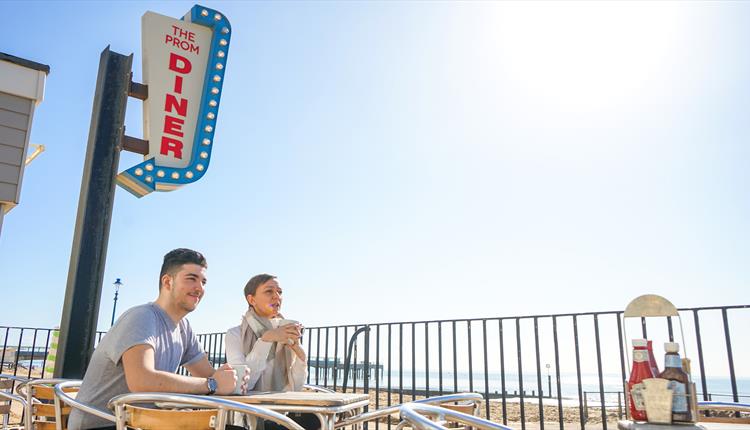Two people sitting outside the diner with a blue sky above.