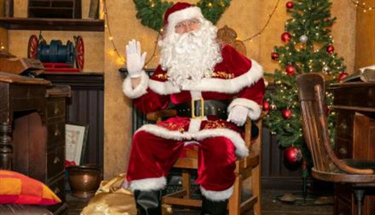 santa sat on a chair with a decorated christmas tree in the background