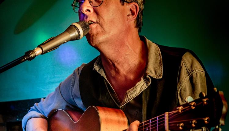 Close up of man with glasses playing guitar and singing into  a microphone