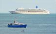 Shot of The Dorset Belle out on the sea with a large cruise liner in the distance.