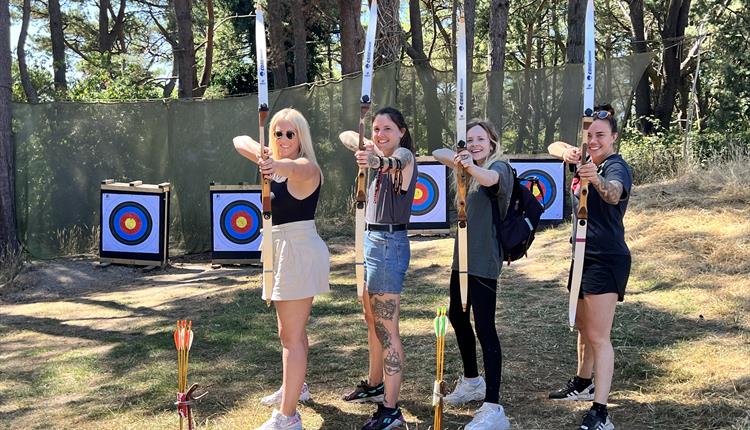 Archery lessons in Dorset with four women holding a crossbow pointing at the camera and smiling