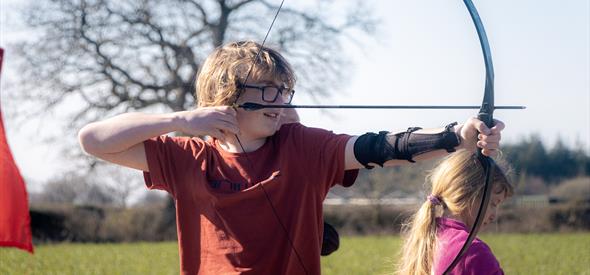 young boy with glasses with a bow and arrow outside 