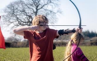 young boy with glasses with a bow and arrow outside