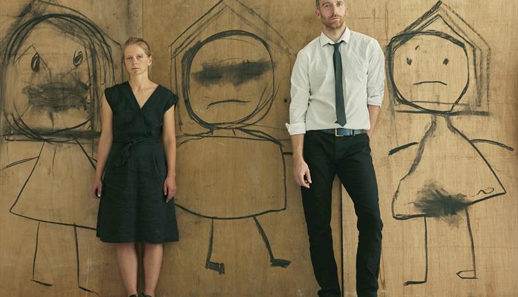 A man and woman standing against a wooden wall