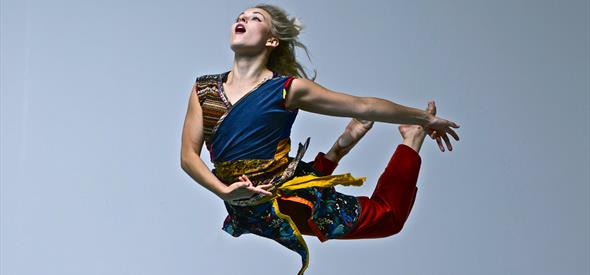A woman in bright clothing leaping mid-dance.