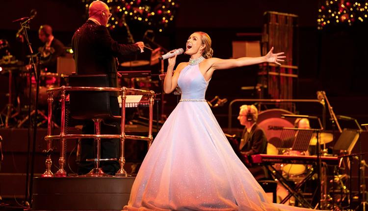 Lady in big white dress singing with an orchestra