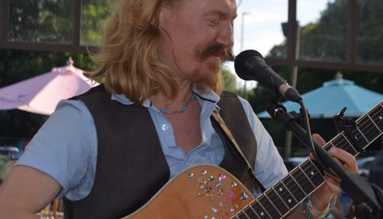 Close up of long haired man with a beard, playing guitar and singing into a microphone