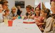 Kids watching a girl blow out her birthday candles