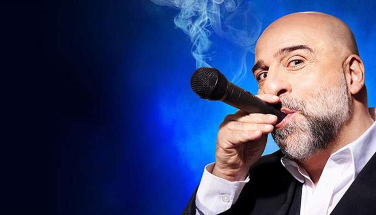 A dark blue back ground. A man holding a microphone to his mouth, as if it were a cigar, with smoke coming out.