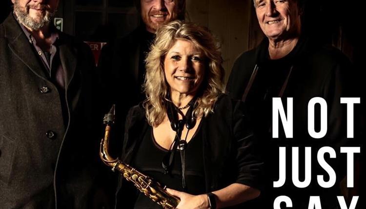 Lady holding a saxophone with long blond hair standing in front of three men all looking at camera