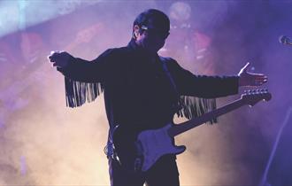 Silhouette of a man in purple and cream coloured smoke holding a guitar