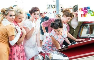 Ladies in vintage clothing standing around vintage car