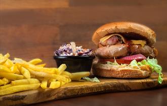 Beefburger, fries and coleslaw on a board