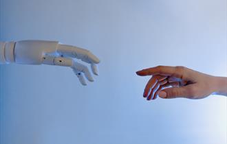 A white robot hand reaching towards a human hand