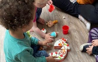 Two children playing with a wooden toy set of various foods.