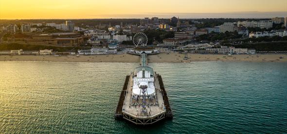 Drone shot of Bournemouth Pier and the surrounding beach area as the sun sets in the distance