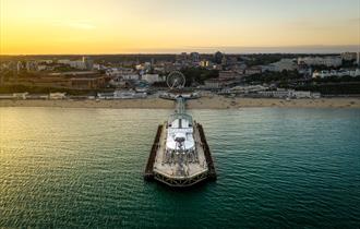 Drone shot of Bournemouth Pier and the surrounding beach area as the sun sets in the distance