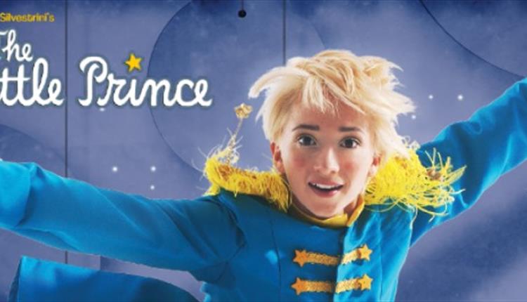 A boy with blonde hair, jumping, wearing a blue jacket with yellow tassels on the shoulder.