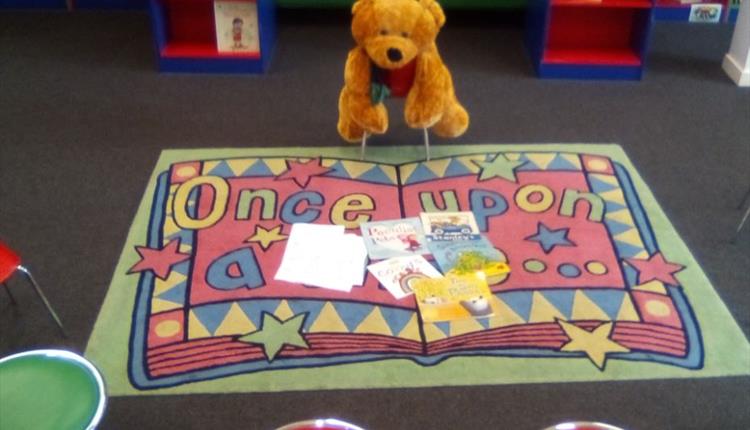 Colourful mat with teddy bear on chair.
