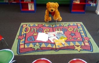 Colourful mat with teddy bear on chair.