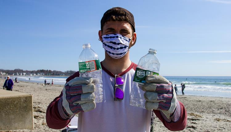 Photo of man holding two plastic bottles on beach, during beach litter pick