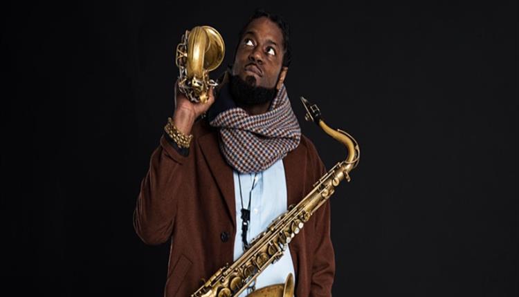 Musician standing looking upwards with a saxophone hanging from his neck and another resting on his shoulder.