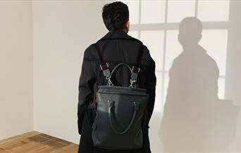 Person with black backpack and dark jacket looking at wall