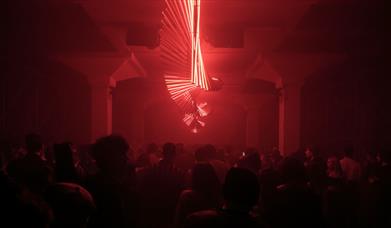 Twisting red neon strip lights in a dark room above a dancing crowd