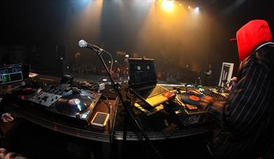 Person in a red hood DJing to a large crowd