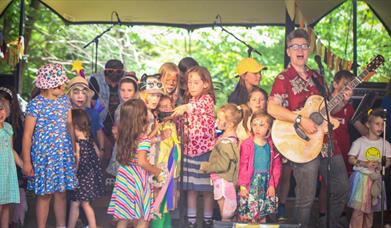 Children on a stage singing with Al Start who is playing the guitar.