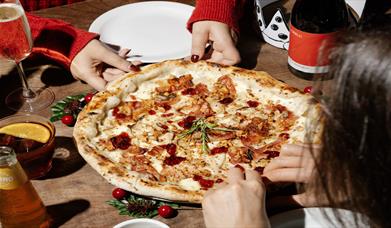 Diners at Franco Manca Brighton enjoying a tasty pizza. Image shows a close up of the pizza being shared by two people wearing red jumpers.