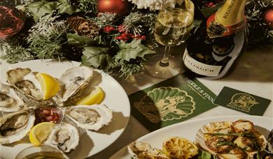 Image shows a platter of fresh seafood at Riddle & Finns in the Lanes. Oysters with lemon wedges next to a platter of scallops, with a bottle of Bolli