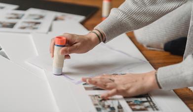 A person with tattoos using a glue stick on paper