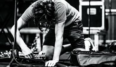 Black and white image of a person plugging in a pedalboard on stage