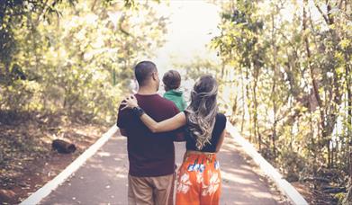 Young family walking in a light forest and carrying their toddler