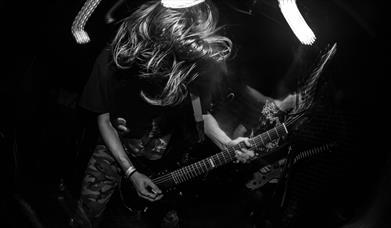 Black and white image of person with wild hair playing an electric guitar