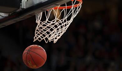 Basketball in the air underneath a basketball hoop